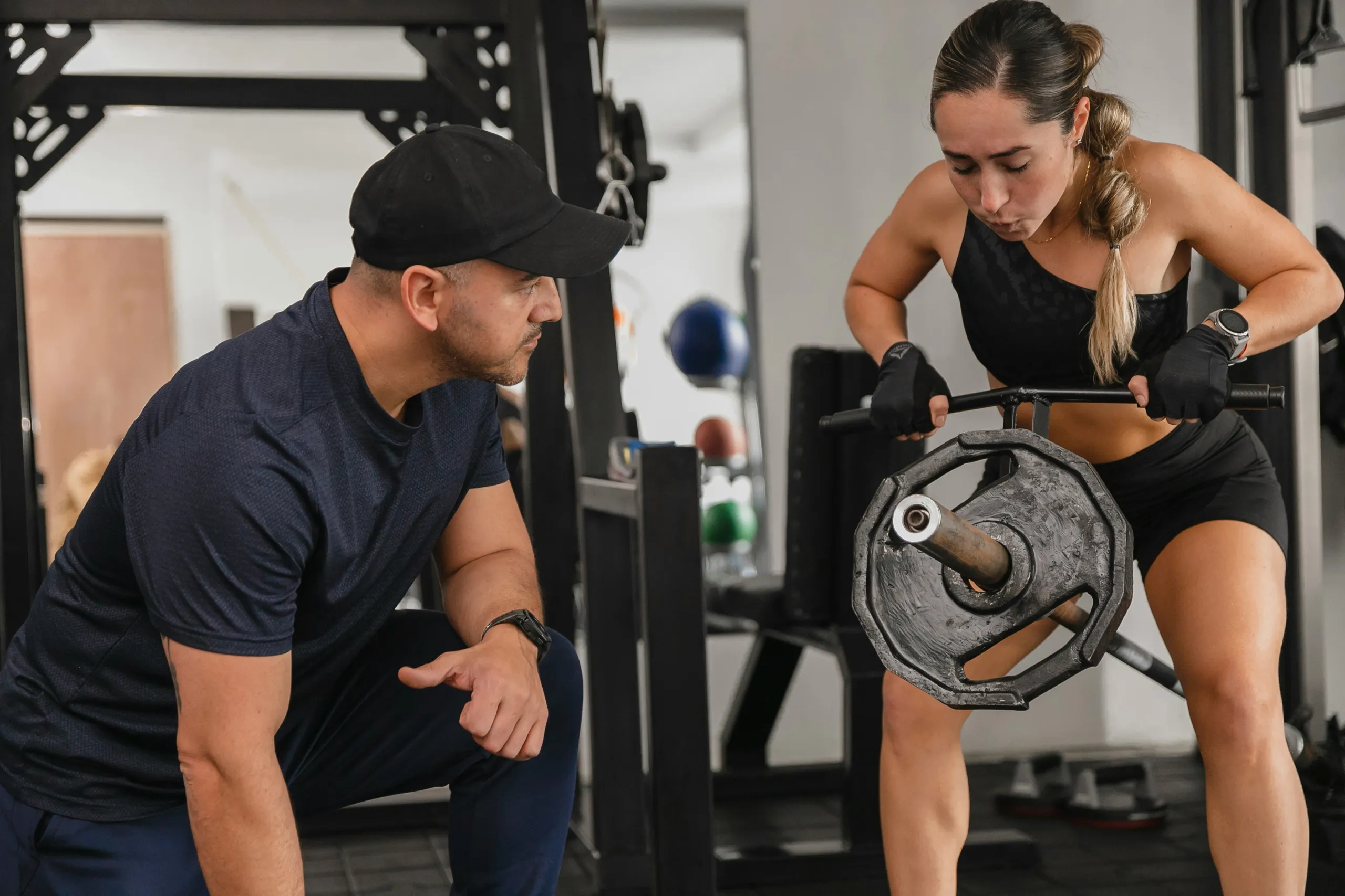 Entrenador asistiendo a una mujer durante un entrenamiento de fuerza con barra